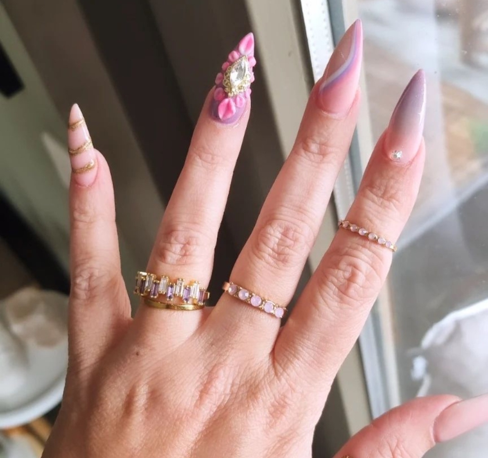 Roze stiletto nagels met een 3D bloem, steentje en gouden ringen